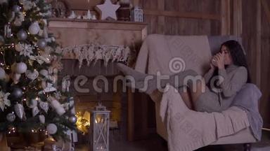 圣诞节，一个女孩坐在圣诞树附近的椅子上喝茶。 高清高清